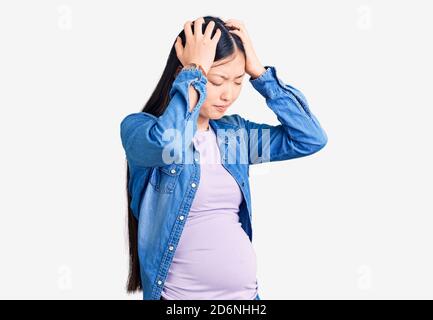 Junge schöne chinesische Frau schwanger erwartet Baby leiden unter Kopfschmerzen verzweifelt und gestresst, weil Schmerzen und Migräne. Hände auf dem Kopf. Stockfoto