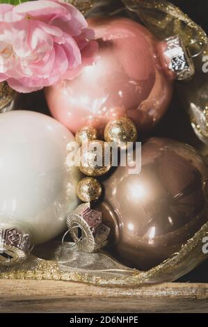 Nahaufnahme von Weihnachtskugeln in einem Holztablett mit goldenen Glitzerkugeln und rosa Nelken. Umrandung des Bildes Stockfoto