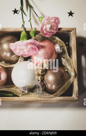 Stillleben von Weihnachtskugeln in einem Holztablett mit goldenen Glitzerkugeln und rosa Nelken verziert. Umrandung des Bildes Stockfoto