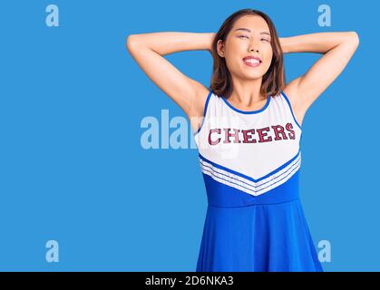 Junge schöne chinesische Mädchen trägt Cheerleader Uniform entspannend und Stretching, Arme und Hände hinter Kopf und Hals lächelnd glücklich Stockfoto