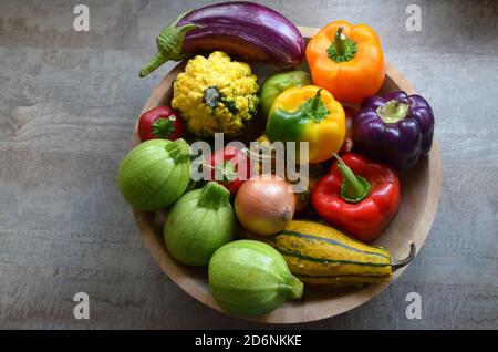 Eine Holzschale mit frischem Bio-Herbstgemüse: Zucchinis, Kürbisse, rote, orange und lila Paprika, Zwiebeln, Auberginen Stockfoto