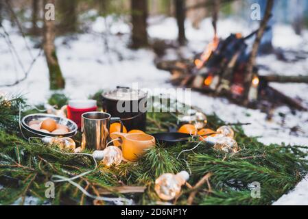 Winterpicknick im Schnee am Lagerfeuer mit Orangen und Tee. Weihnachtsgirlanden auf Tannenzweigen