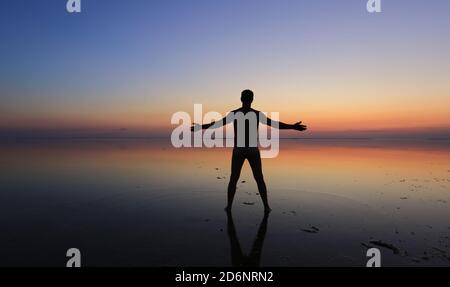 Der Mensch steht im Wasser an der Küste mit seinem Arme vor dem Hintergrund des Sonnenuntergangs ausgestreckt Stockfoto