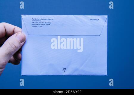 Paris, Frankreich - Mar 14, 2018: POV männliche Hand hält agaisnt blauen Hintergrund Papier enevlope mit Adresse von TransferWise in Großbritannien Stockfoto