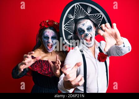 Schönes Paar trägt Tag der Toten Kostüm gestikuliert als Zombie über isolierten roten Hintergrund. Stockfoto