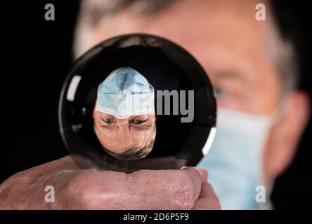 Senior Mann trägt Gesichtsmaske gegen Coronavirus und spiegelt sich in Wahrsagerei Glaskugel. Konzept der Menschen, die Verantwortung bei der Wahl wählen Stockfoto