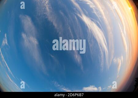 Rauchschichten aus einem nahegelegenen Waldfeuer geben der untergehenden Sonne über den Cascade Mountains mit wispy weißen Wolken am tiefblauen Himmel ein orangefarbenes Leuchten. Stockfoto