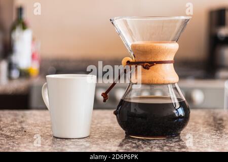 Hispanische Barista gießt Kaffee in eine weiße Tasse in der Familienküche. Schwarze Frau hält gießen über Kaffeekanne am Morgen Stockfoto