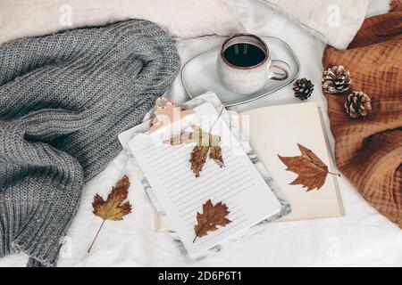 Herbstfrühstück stilles Leben. Tasse Kaffee, offenes Buch und Notizblock mit bunten Ahorn- und Eichenblättern. Weißer Leinenhintergrund. Leinenkissen und grau Stockfoto