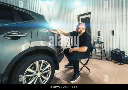 Details zum Fahrzeug. Arbeiter Polieren mit Mikrofaser Handtuch hinten Optik Licht des Autos in der Auto-Service-Station. Stockfoto