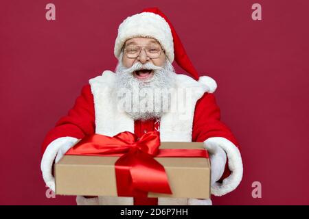 Glücklicher Weihnachtsmann hält präsent, lachend, auf rotem Hintergrund stehend. Stockfoto
