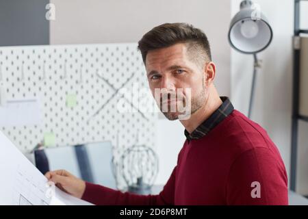 Porträt von bärtigen reifen Mann mit Blaupausen und Blick auf die Kamera während der Arbeit in der Architektur oder Bauindustrie, kopieren Raum Stockfoto