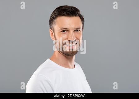 Hübscher Kaukasianer mittleren Alters, der vor der Kamera auf Grau lächelt Stockfoto