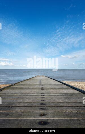 Ein langer hölzerner Steg ragt in das ruhige blaue Meer vom Strand an Whitstable Beachfront in Kent, England. Stockfoto