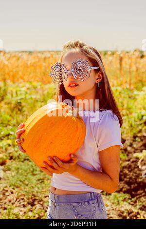Teenager Mädchen und Kürbis im Gemüsegarten. Ein Mädchen mit einem Kürbis in den Händen trägt eine Brille für Halloween. Stockfoto