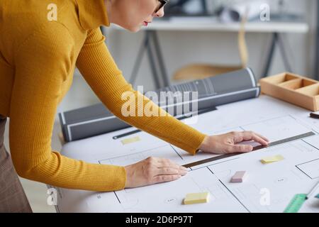 Abgeschnittene Seitenansicht Porträt einer unerkennbaren Architektin, die Blaupausen zeichnet, während sie sich am Arbeitsplatz auf den Schreibtisch lehnt, Raum kopieren Stockfoto