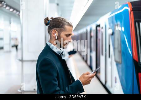 Junger Mann liest eine SMS, während er auf der U-Bahn-Plattform steht. Stockfoto