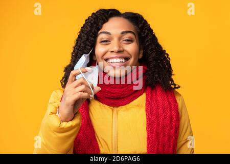 Happy African Lady Abheben Schützende Gesichtsmaske, Gelber Hintergrund Stockfoto