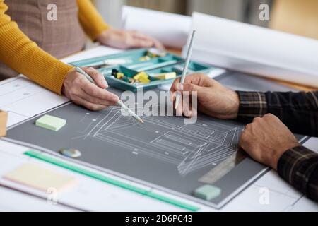 Nahaufnahme von zwei nicht erkennbaren Architekten, die auf den Grundriss zeigen, während sie an Bauplänen am Arbeitsplatz arbeiten, Platz kopieren Stockfoto