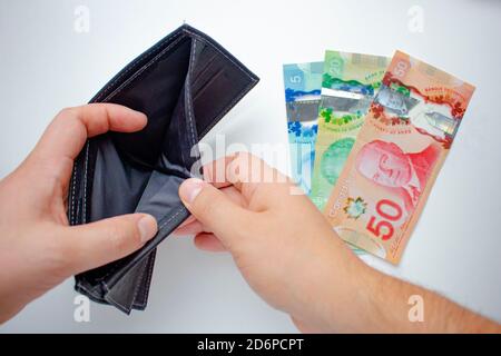 Eine Person, die eine leere Brieftasche öffnet und kanadische Dollar auf weißem Hintergrund ausgibt. Konzept: Spending Savings. Stockfoto