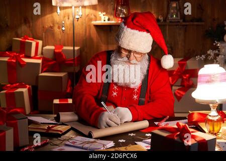 Happy Santa Claus arbeitet an Heiligabend sitzen am heimischen Tisch. Stockfoto