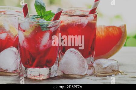 Roter Cocktail mit Grapefruit und Eis in Form eines Herzens auf einem grünen natürlichen Hintergrund, selektiver Fokus und getöntes Bild Stockfoto