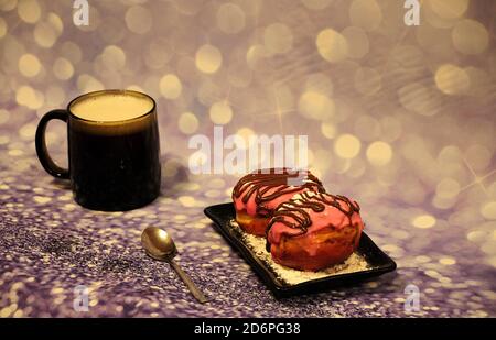 Dunkler Cappuccino Becher und Teller mit zwei Donuts in rosa Glasur und Puderzucker auf grauem abstraktem Hintergrund. Nahaufnahme. Stockfoto