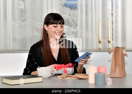Schöne junge Frau mit einem blauen Umschlag und einer silberumhüllten Geschenkbox auf einem unfokussierten Hintergrund. Geschenke und Glück Konzept. Stockfoto