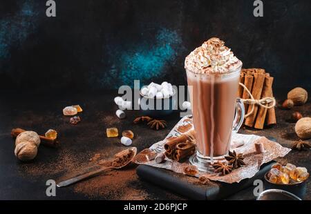 Heißer Kakao-Drink im Winter in hohem Glas mit Eiscreme und Sahne auf schwarzem Tisch. Dunkelblauer Hintergrund. Speicherplatz kopieren Stockfoto