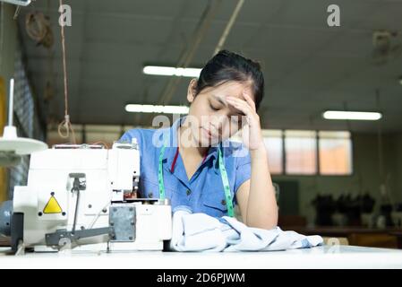 Schneiderinnen halten sich beim Nähen wegen Stress am Kopf Kleidung in der Bekleidungsindustrie Stockfoto
