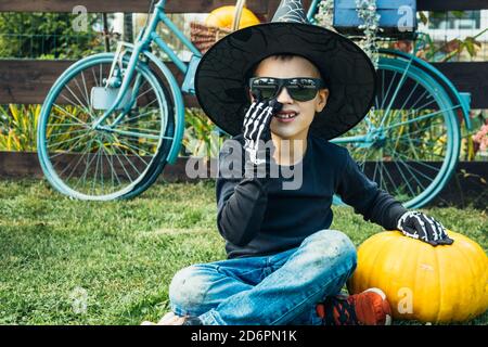 Der Junge mit Kürbis in Kundenhut und Handschuhen sitzt auf der Straße. Frohe halloween. Halloween Kinder. Stockfoto