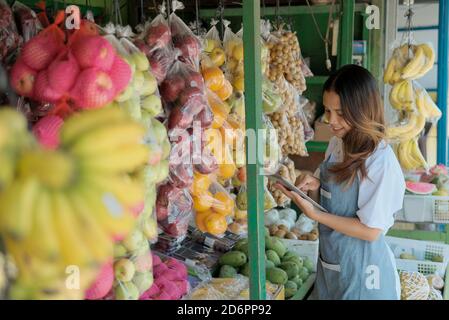 Lächelnde Frau Shop Assistentin in Schürze stehend mit Tablet als nächstes Zu Bio-Früchten im Stall Stockfoto