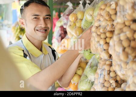 Shop Assistant Arrangieren hängende Kunststoff-Obst-Verpackung in einem Obst Kaufen Stockfoto