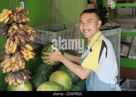 Asiatisches Männchen in einer Schürze hält Watemelon in einem Obststände, frisches Obst-Konzept Stockfoto