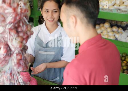 Ein Mann, der Lebensmittel in einem Supermarkt kauft und Hilfe von erhält Ein Verkäuferin Stockfoto