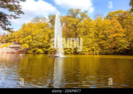 Sonniger Herbsttag in einem Laubpark. Hoher Brunnen in der Mitte des Teiches Stockfoto