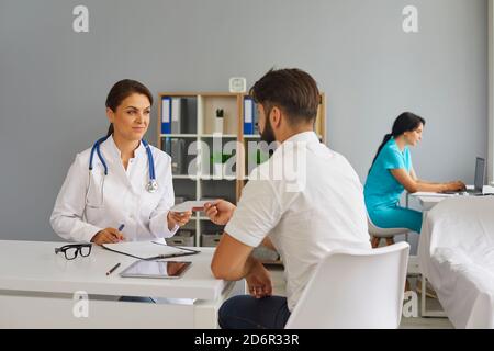 Der Arzt gibt dem Patienten ein Rezept, während er am Tisch im Büro der Klinik sitzt.Medizinische Beratung. Stockfoto