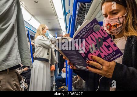 London, Großbritannien. Oktober 2020. Raum einnehmen - eine Frau liest ein Buch mit passendem Titel, auch wenn das Thema etwas anders ist. Die Passagierzahlen bleiben in der U-Bahn zurückgegangen, steigen aber jetzt an und die Züge sind moderat beschäftigt, insbesondere zur Hauptverkehrszeit. Genau wie die Regierung beginnt, ihre Coronavirus-Leitlinien (covid 19) wieder zu straffen. Diejenigen, die Reisen meist tragen Masken, nachdem sie obligatorisch auf öffentlichen Verkehrsmitteln. Kredit: Guy Bell/Alamy Live Nachrichten Stockfoto