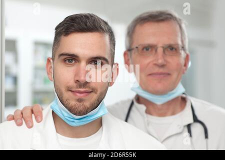 Lächelnde junge und reife Ärzte stehen vor einem Operationsraum - Fokus auf den jungen Arzt Stockfoto