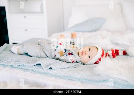 Das erste Weihnachten des Kindes. Ein niedlicher kleiner Junge in einem Weihnachtsmütze. Auf dem Bett liegend. Die Aussicht von oben. Weihnachtskonzept. Stockfoto