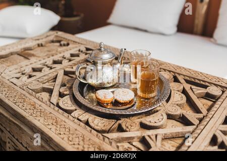 Traditioneller marokkanischer Minztee mit Plätzchen auf silbernem Tablett auf geschnitztem Holztisch. Schöner Vintage-Stil, Gastfreundschaft in Marokko. Stockfoto