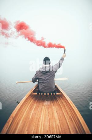 Mann im Kanu mit Rauchbombe, um seine Position zu signalisieren Auf dem nebligen See Stockfoto