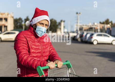 Mann in einer medizinischen Maske mit einem Weihnachtsmann Hut Mit einem Warenkorb Stockfoto