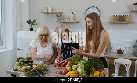 Ältere Großeltern Paar mit Enkelin in der Küche. Ältere Mann und Frau hören Rezept, Ratschläge von Mädchen mit digitalen Tablette gesunde Ernährung. Rohkost Essen Diät. Welt vegan Tag Stockfoto