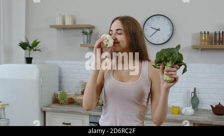 Glücklich jung lächelnd teen Mädchen in der Küche zu Hause hält Brokkoli und Blumenkohl in ihren Händen. Empfehlen Essen rohe pflanzliche Lebensmittel. Gesunde Ernährung Ernährung und Gewichtsverlust Konzept Stockfoto