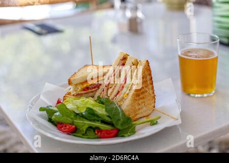 Club Sandwich mit einem Glas Bier auf einem Tisch. Fast Food Stockfoto