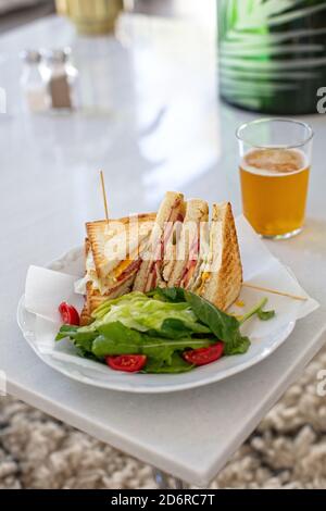 Club Sandwich mit einem Glas Bier auf einem Tisch. Fast Food Stockfoto