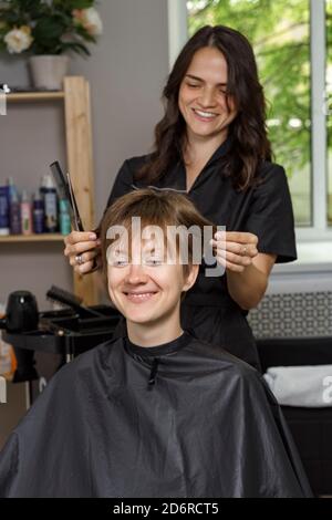 Schöne Friseur Frau in schwarzen Uniform schneidet Haare der jungen Frau. Schönheitssalon Konzept Stockfoto