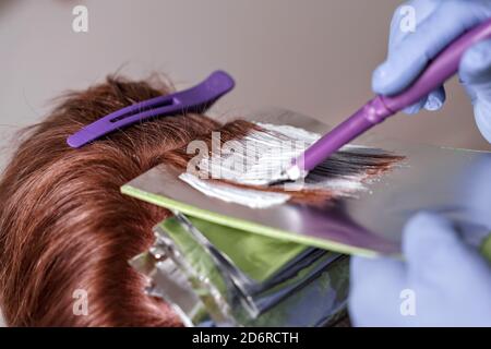 Der Prozess des Färbens von rotem Haar mit Folie. Der Meister trägt die Komposition mit einem Pinsel auf das Haar des Kunden Stockfoto