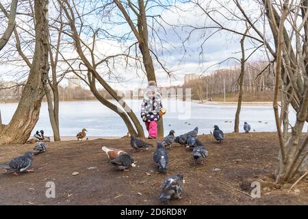 Ein kleines Mädchen hält Brot in den Händen und ernährt sich Tauben und Enten am gefrorenen Teich Stockfoto